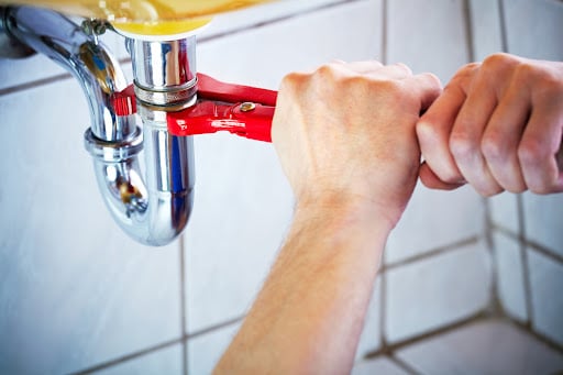 adjustable-wrench Plumber hands holding wrench and fixing a sink in bathroom.