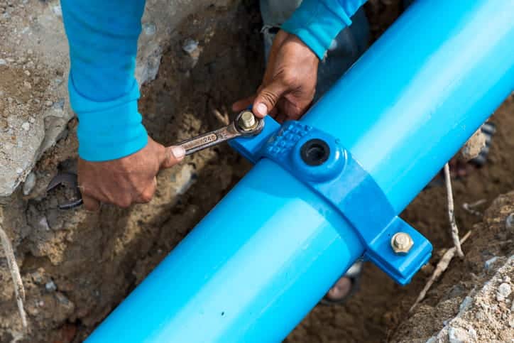 Man using a large wrench on blue water pipes.